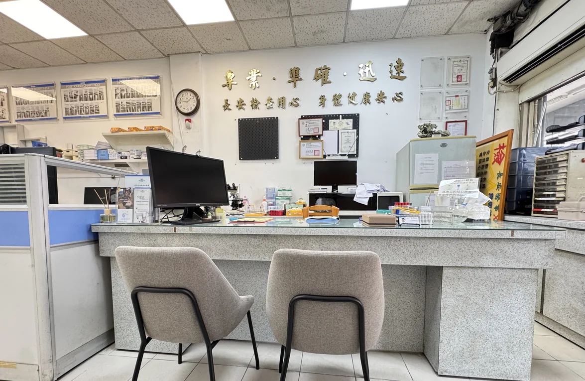 長安醫事檢驗所店內實景：受理櫃檯、兩張採檢座椅與電腦設備，牆面為「專業、準確、迅速」與「長安檢查用心　身體健康安心」字樣