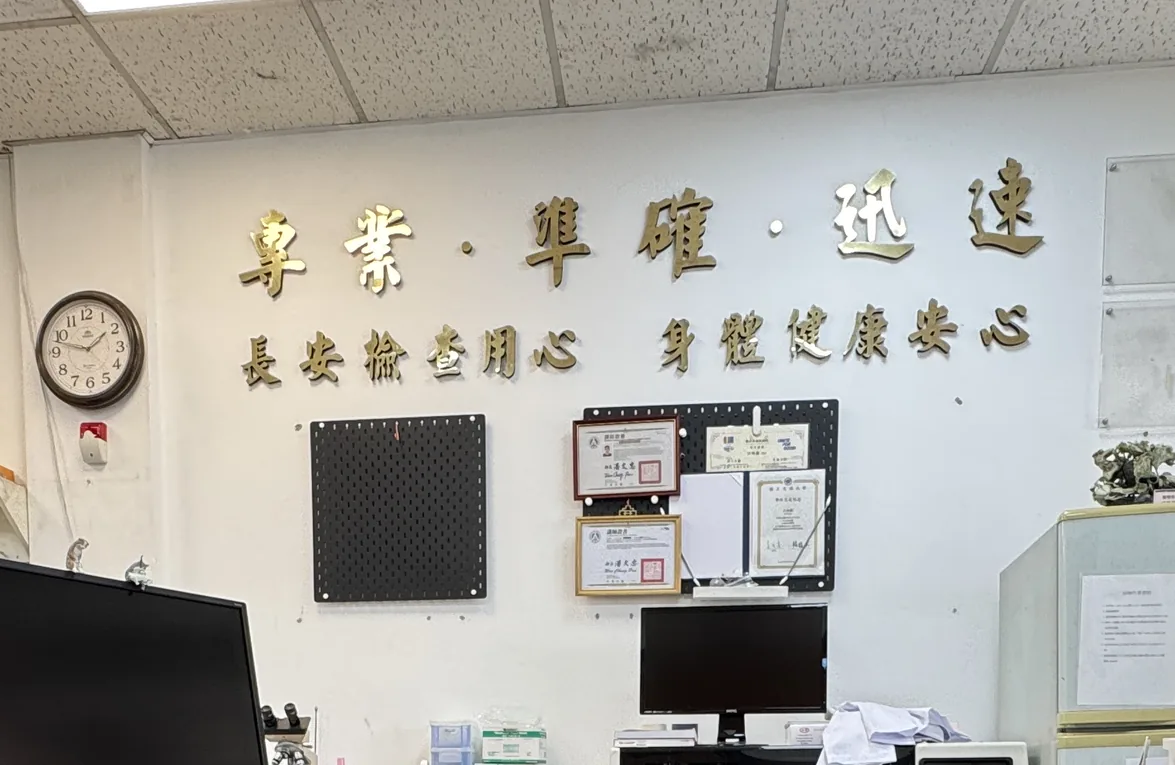 長安醫事檢驗所店內實景：櫃檯上方牆面的「專業、準確、迅速」與「長安檢查用心　身體健康安心」字樣，以及櫃檯上的電腦設備與檢驗耗材